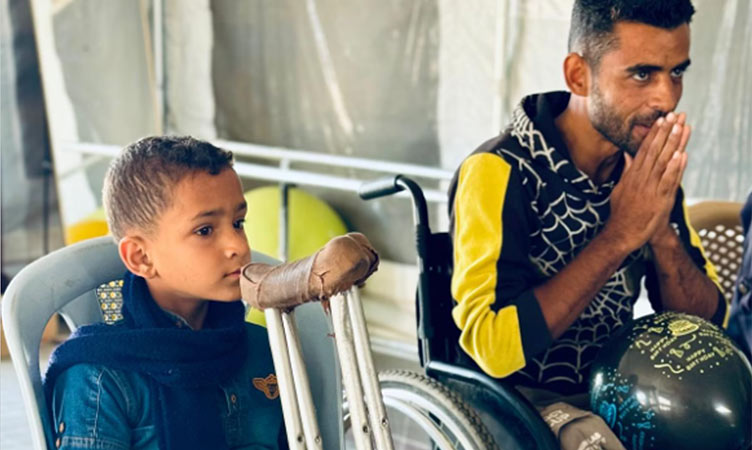 A child and adult in wheelchairs in war-torn district