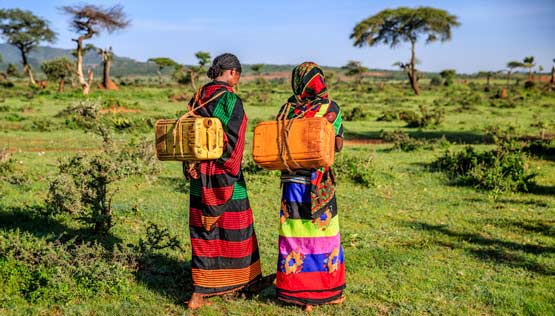 Two women with supplies walk in green field in Africa