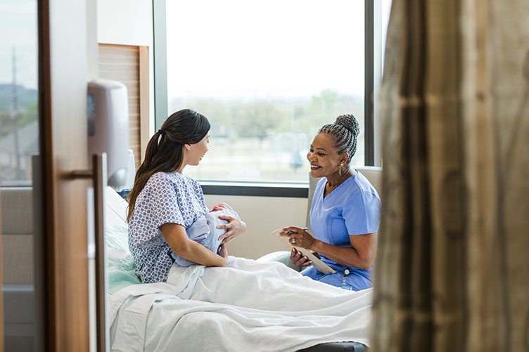 A nurse, a mother and her baby on a maternity hospital bed.