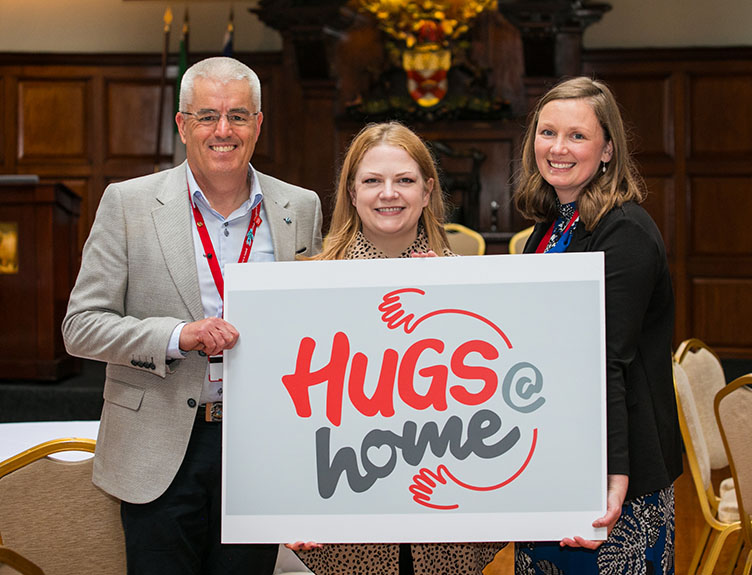 Three people with a Hugs@home sign