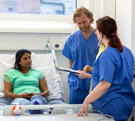 Two clinicians with a patient who is in a hospital bed.