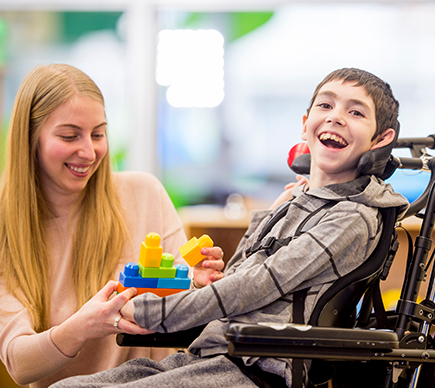 A young wheelchair user playing with building blocks next to a woman.