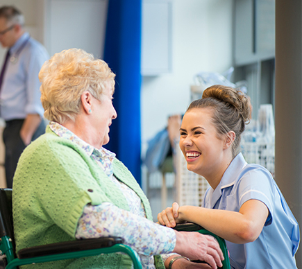 A female nurse shares a joke with an elderly woman in a wheelchair.