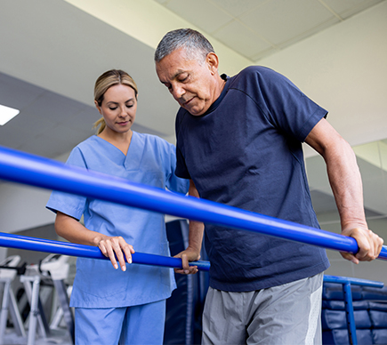 A female nurse assisting an elderly man to walk using handrails.