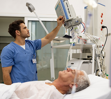 A male medical professional operating digital equipment at a patient's bedside.