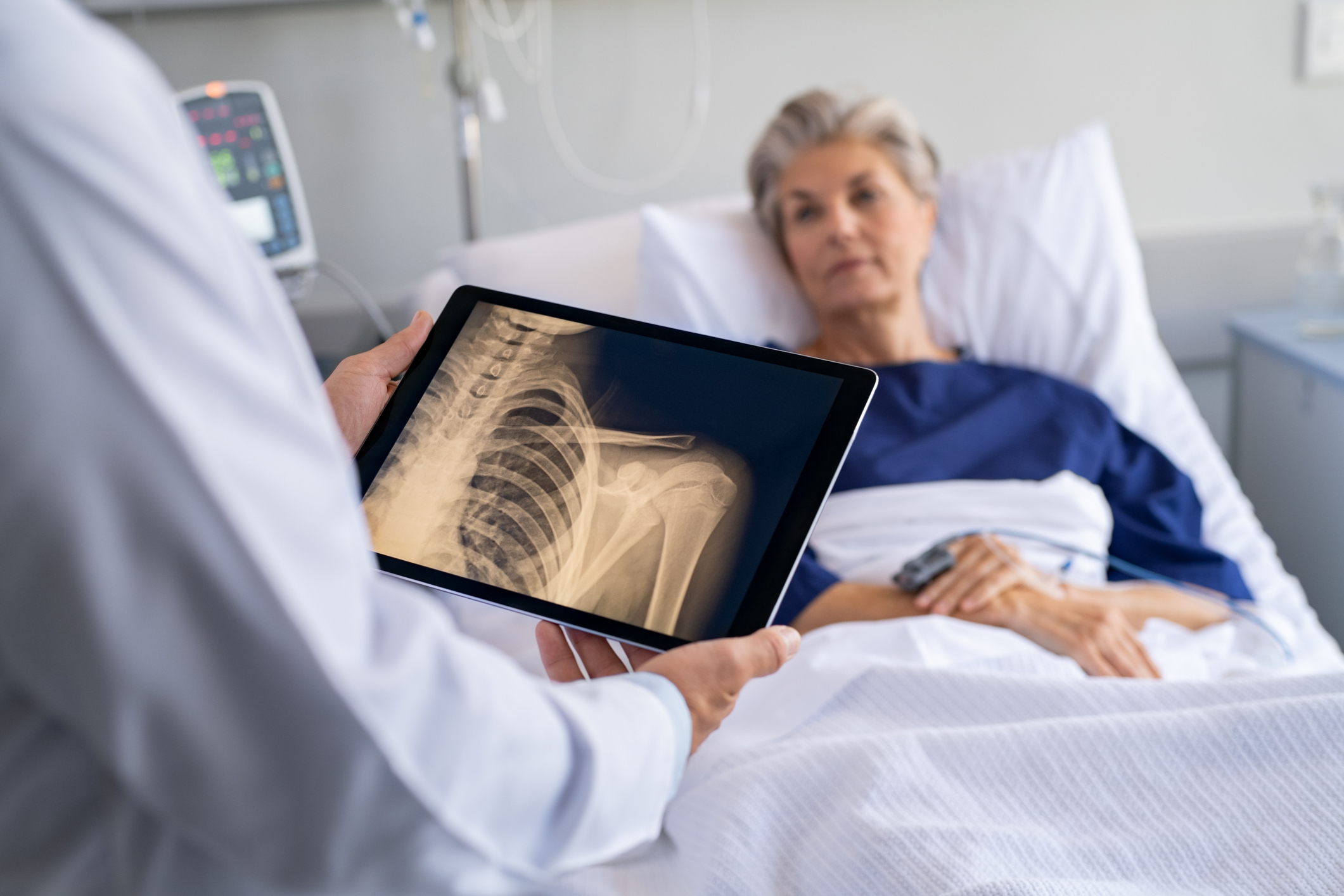 Patient in bed as doctor reviews X-ray